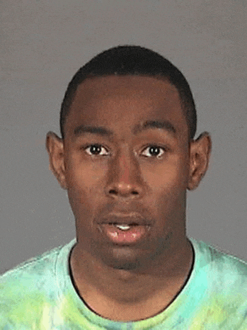 tyler the creator is wearing a tie dye t-shirt and making a funny face .