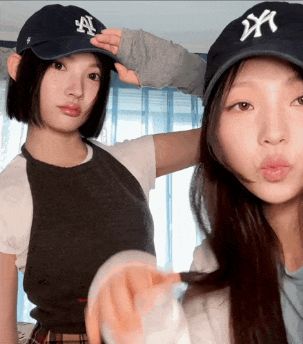 two young women wearing ny hats pose for a picture