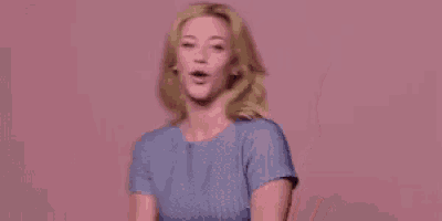 a woman is standing in front of a pink wall and holding her hair in a ponytail .