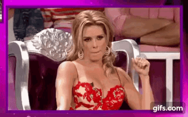 a woman in a red dress is sitting in a chair with her fist up .