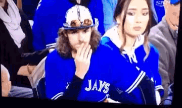 a man wearing a jays jersey looks at a woman