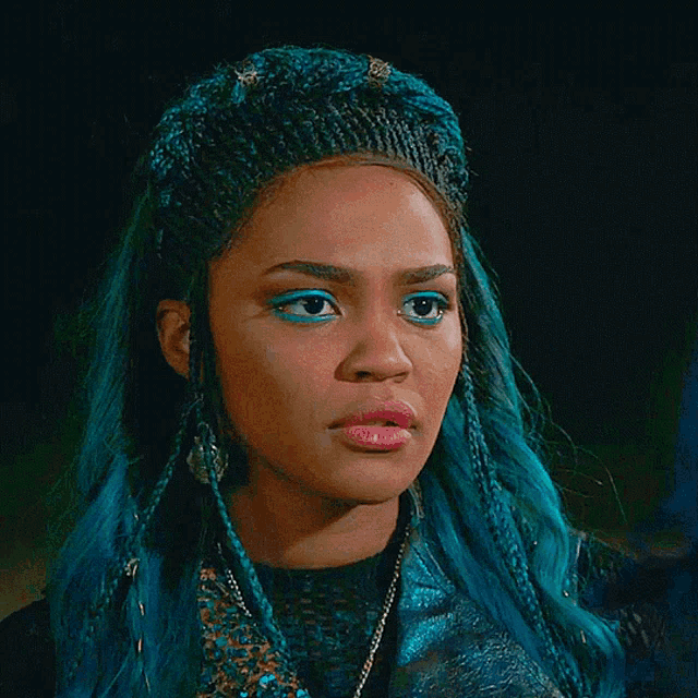 a woman with blue hair is wearing a knitted hat