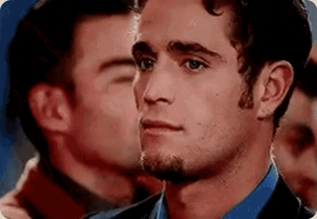 a close up of a man 's face with a man behind him kissing him on the cheek .