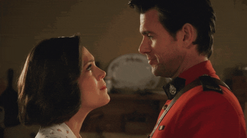 a man in a red uniform is kissing a woman in a white shirt
