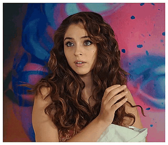 a woman with long curly hair is holding her hair in front of a painting .