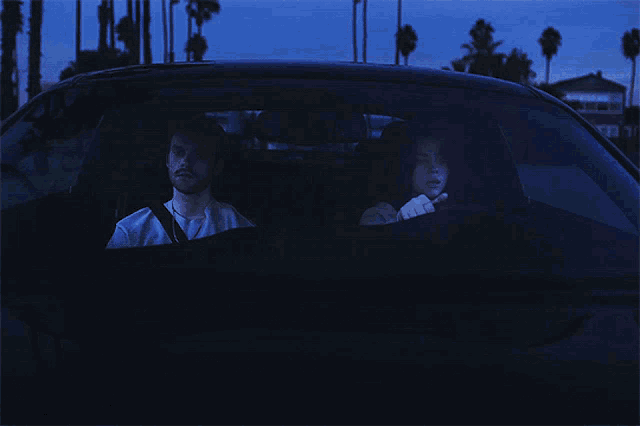a man and a woman are sitting in a car with a stop sign in the background