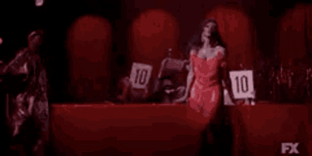 a woman in a red dress is holding a sign that says `` 10 '' on it .