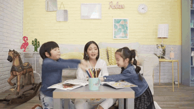 a woman sits at a table with two children and a mug of colored pencils on it