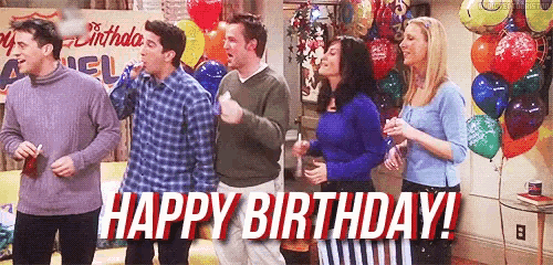 a group of people are standing in a room with balloons and a sign that says `` happy birthday '' .