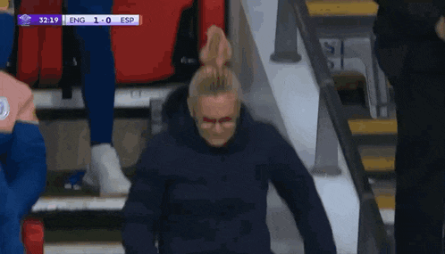 a woman wearing glasses and a face mask walks down the stairs during a soccer game