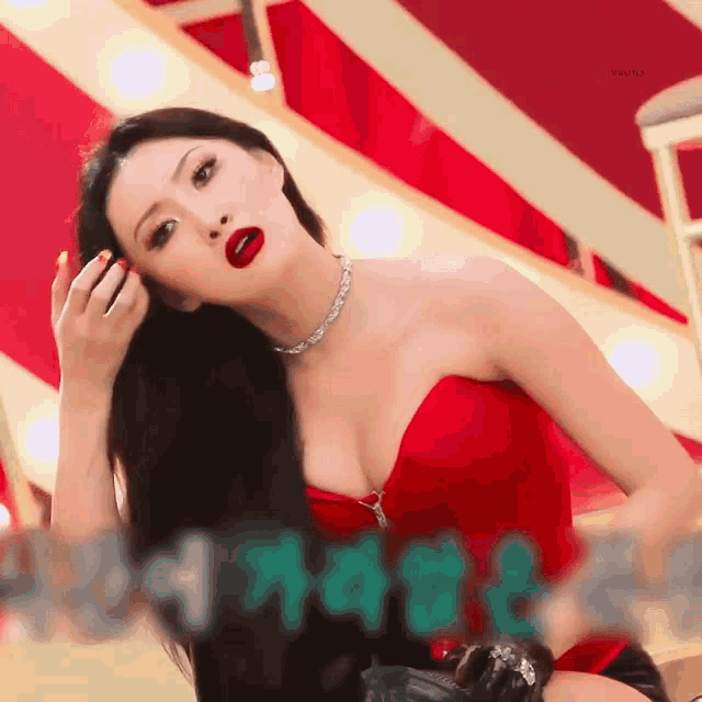 a woman wearing a red strapless top and a necklace is sitting on a stage .
