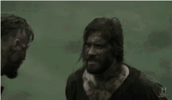 two men are standing next to each other in a field and one of them is covered in blood .
