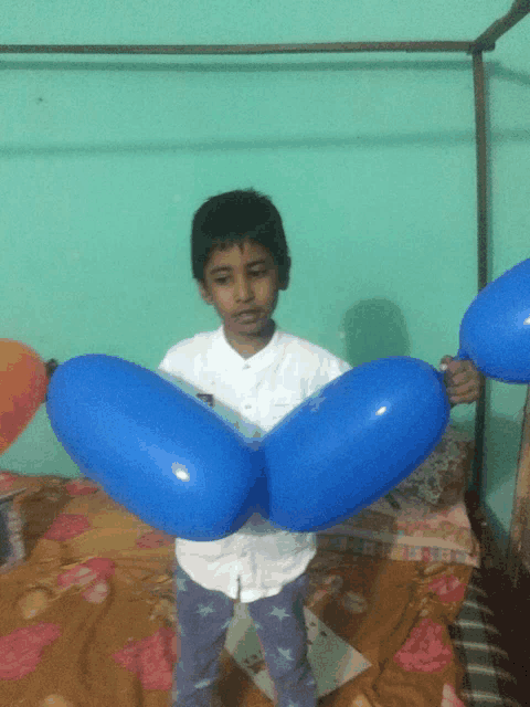 a boy is holding two blue balloons in front of a bed