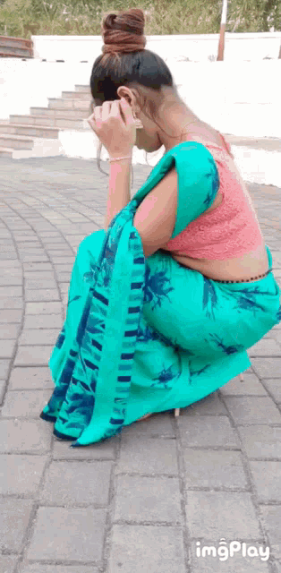 a woman in a blue saree and a pink blouse is kneeling down