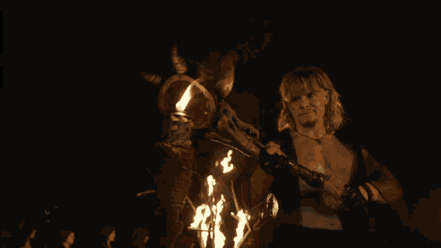 a man with a tattoo on his chest is standing next to a statue of a man with horns