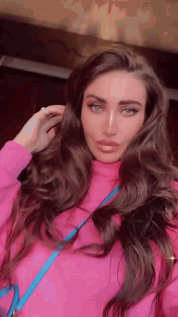 a woman with long hair is wearing a pink sweater and a blue bag .