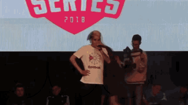 a man is standing on a stage with a microphone in front of a large screen that says series 2018 .