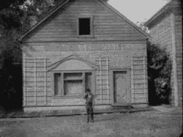 a black and white photo of a man standing in front of a house
