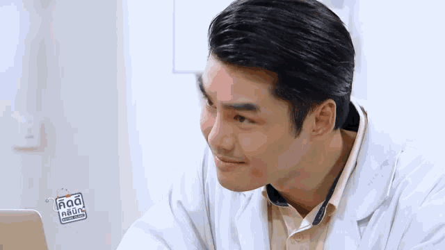 a man in a lab coat is sitting in front of a laptop computer and smiling .