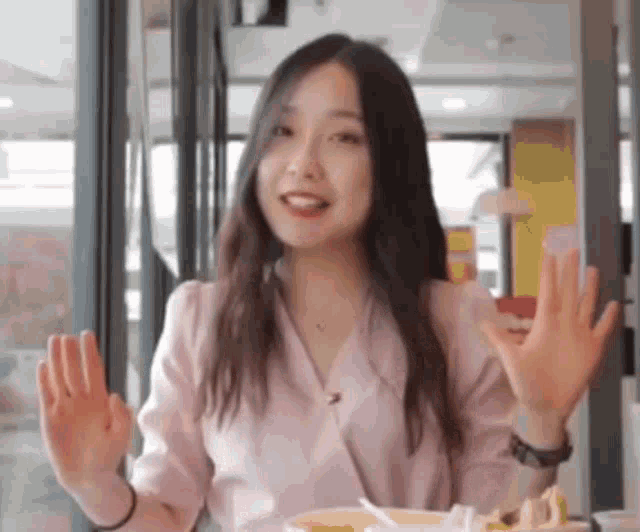 a woman in a pink shirt is sitting at a table with her hands outstretched .
