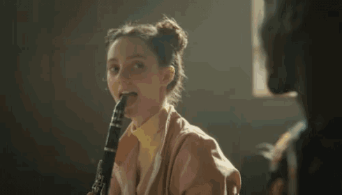 a woman playing a clarinet with a man behind her