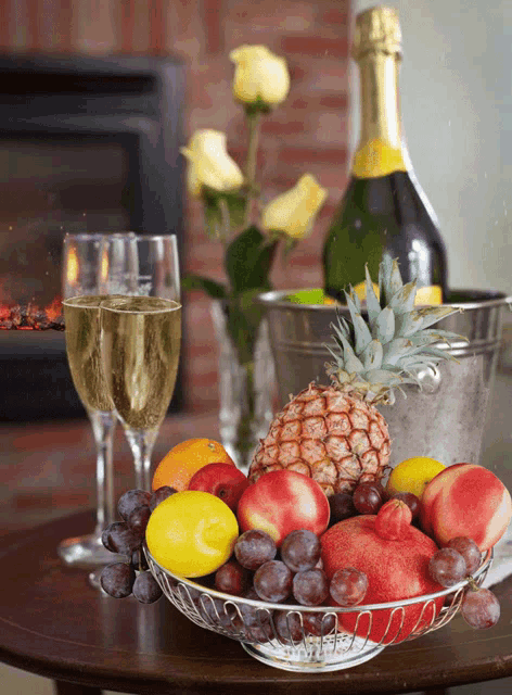 a basket of fruit sits on a table next to two glasses of champagne and a bottle of champagne