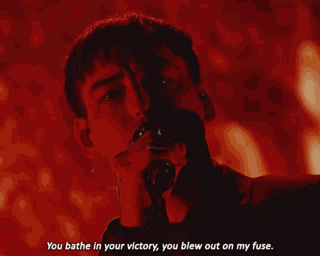 a man singing into a microphone with the words you bathe in your victory you blew out on my fuse below him