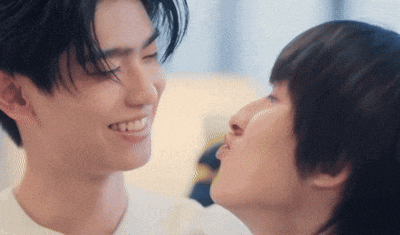 a man is kissing another man on the cheek while they are looking at each other .
