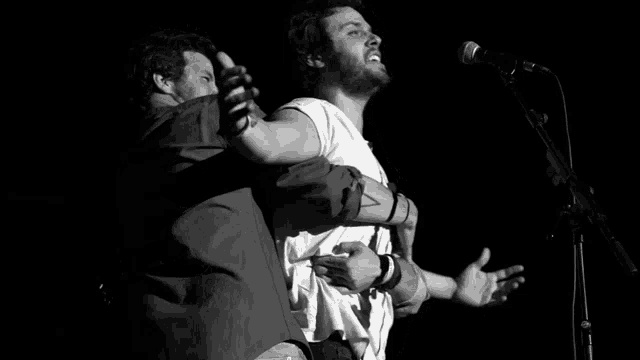 a man with a tattoo on his arm is hugging another man while singing into a microphone