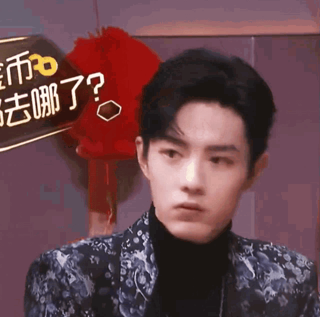 a young man wearing a floral jacket and a black turtleneck is looking at the camera .