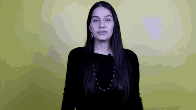 a woman wearing a black sweater and a pearl necklace is standing in front of a yellow wall