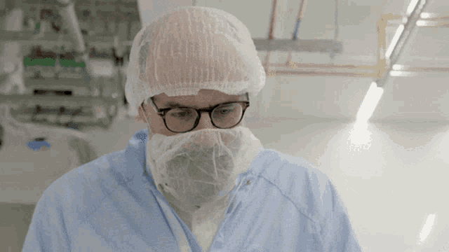 a man with glasses and a beard is wearing a surgical gown and a white cap
