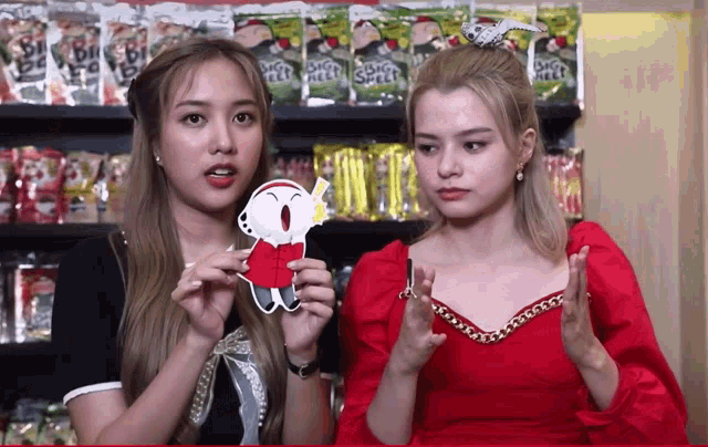 two girls are standing in front of a shelf of snacks and one of them is holding a piece of paper