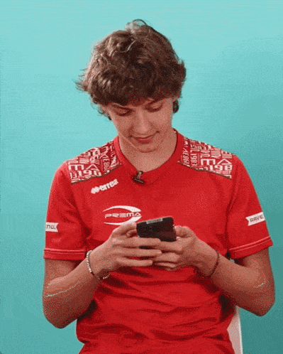 a young man wearing a red errea shirt is looking at his phone