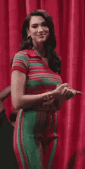 a woman in a striped shirt and green pants is standing in front of a red curtain