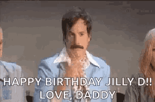 a man with a mustache is sitting in front of a group of people and saying `` happy birthday jilly d ! love daddy ''