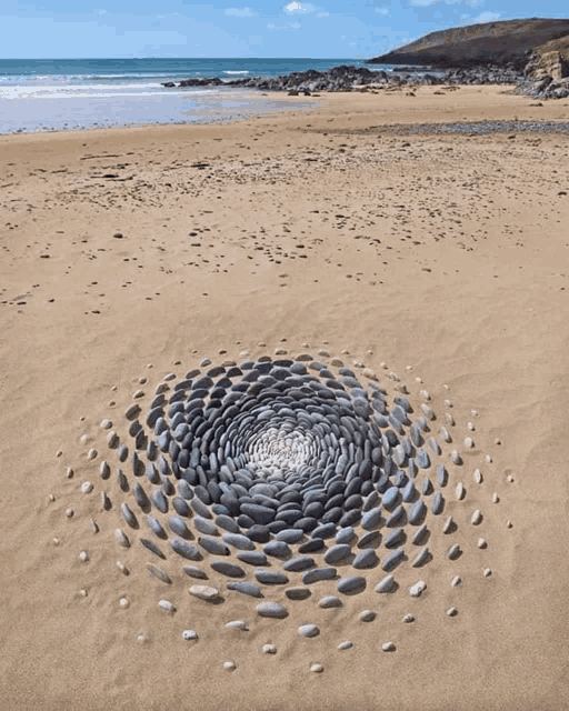 a circular pattern of rocks on a sandy beach with the ocean in the background