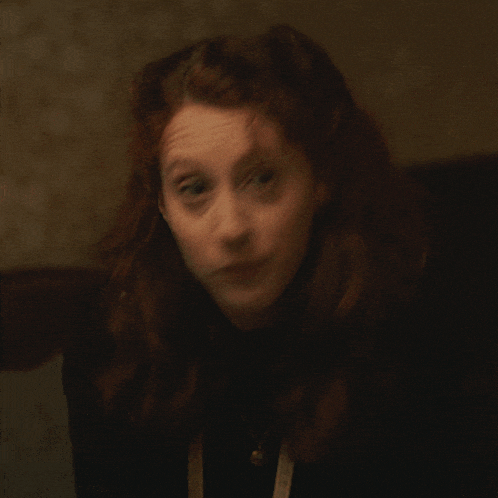 a woman with red hair and a tape measure around her neck looks up at something