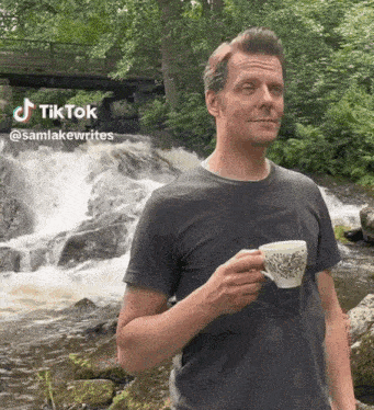 a man is standing in front of a waterfall holding a cup of tea .