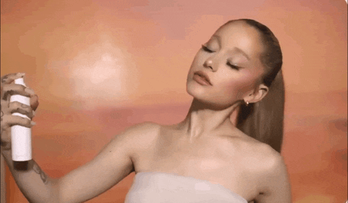 ariana grande is holding a spray bottle in her hand and applying it to her face .