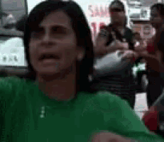 a woman in a green shirt is making a funny face while standing in front of a crowd of people .