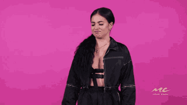 a woman in a black jacket giving a thumbs up on a pink background