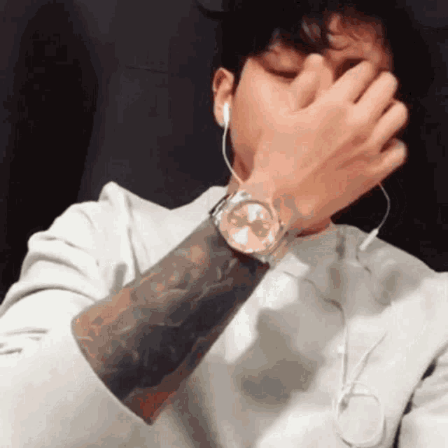 a man with a tattoo on his arm wearing a watch covering his face .