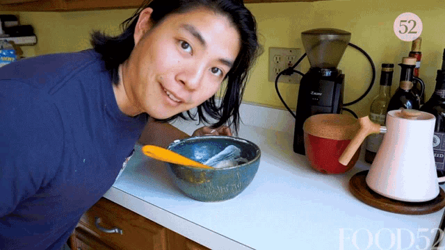 a man in a blue shirt is standing in front of a bowl with a spoon in it and the number 52 on the corner