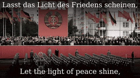 a large crowd of people are gathered in front of a large red banner that says ddr let the light of peace shine