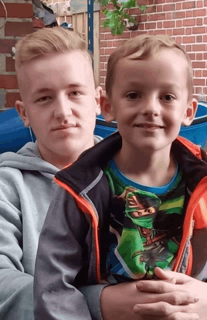a boy wearing a lego ninjago shirt is holding another boy