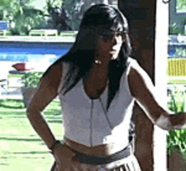 a woman in a white crop top and skirt is standing in front of a window .