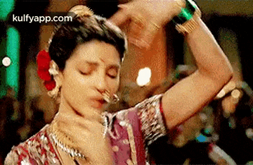 a woman in a sari is dancing with her eyes closed and a flower in her hair .
