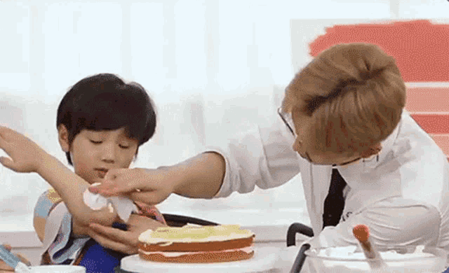 a man is helping a little boy decorate a cake on a table .