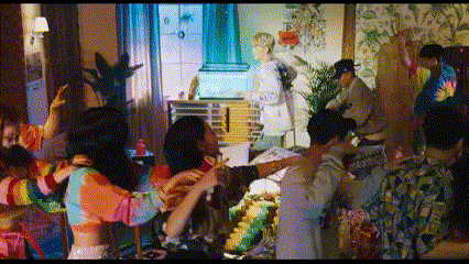 a group of people are dancing in a room with a man standing in the background .